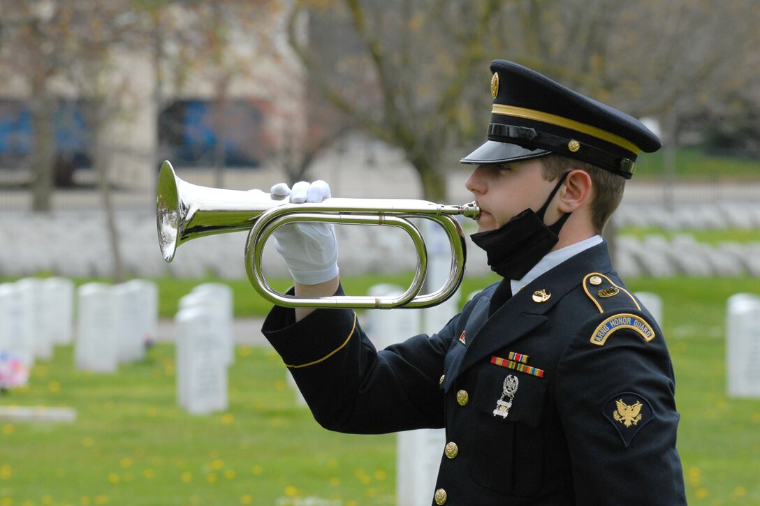 A military bugler plays taps during a funeral in a graveyard.