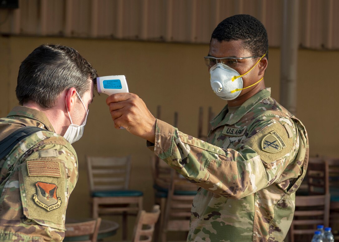 A soldier takes a service member’s temperature.