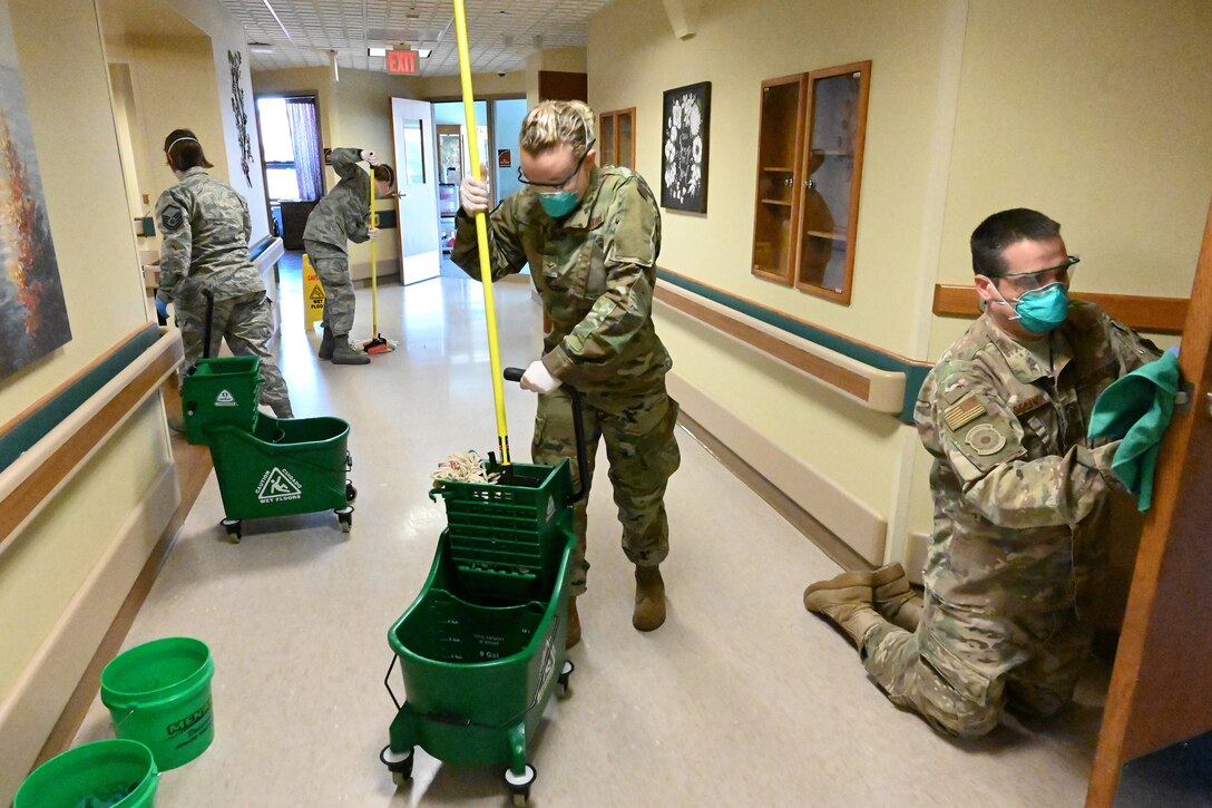 Four North Dakota Air National Guard members wear personal protective equipment as the wipe and mop a hallway using sanitizing liquid at a congregate living facility Fargo, N.D., May 18, 2020.