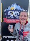 Soldier wearing a hoodie poses with her medal in front of an Army Ten Miler poster.