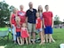 Two grandparents, a husband and wife and their four kids smile wearing red, white and blue at a 4th of July Ceremony.