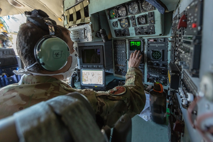 A man in a military uniform interacts with a computer system in the cockpit of an aircraft.