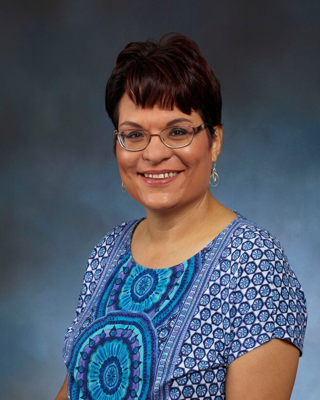 Annette Reggio wearing a blue shirt with a blue professional background.