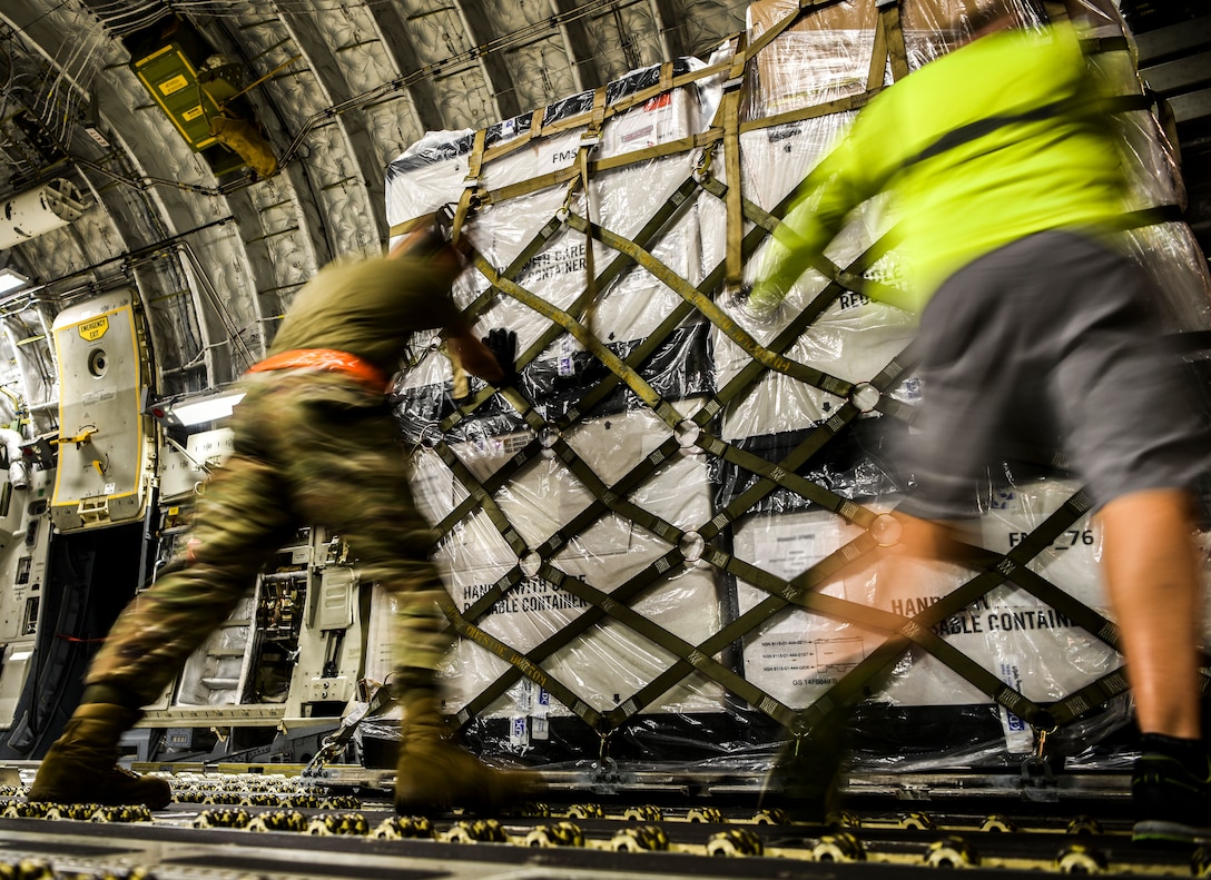 Two men position a pallet of boxes inside an aircraft