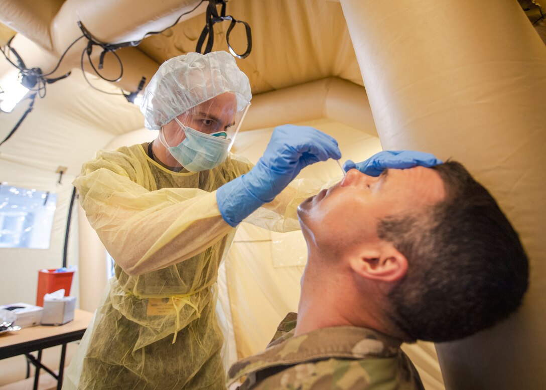 A medic wearing pushes a testing swab into a soldier's nose