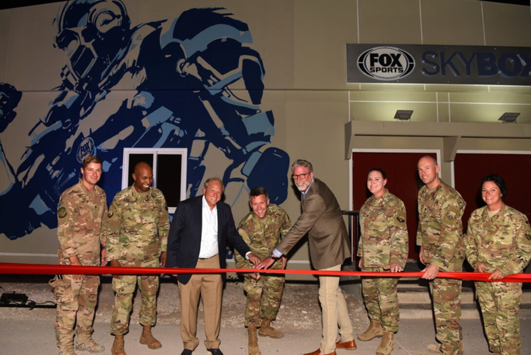 Brig. Gen. Daniel Tulley, 379th Air Expeditionary Wing commander, Larry Jones FOX Sports executive vice president and Gary Hartley, executive vice president, graphics, and creative director and 379th AEW leadership members cut the ribbon for the FOX Sports Skybox grand opening at Al Udeid AB, Qatar on Aug. 10, 2019. (U.S. Air Force photo by Staff Sgt. Ashley L. Gardner)