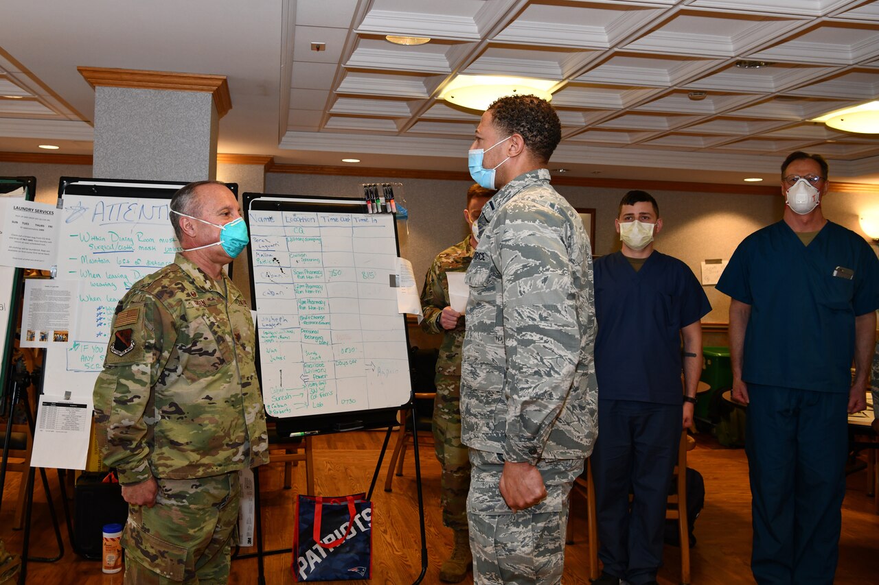 Two officers wearing masks stand at attention during a ceremony as other airmen and some civilians look on.