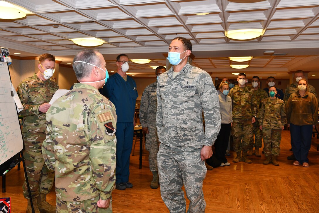 Two officers wearing masks stand at attention during a ceremony as other airmen and some civilians look on.