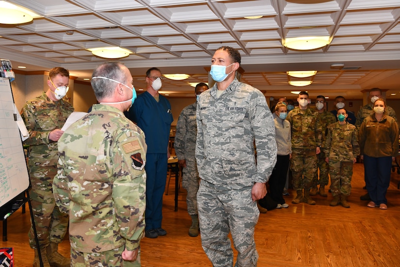 Two officers wearing masks stand at attention during a ceremony as other airmen and some civilians look on.