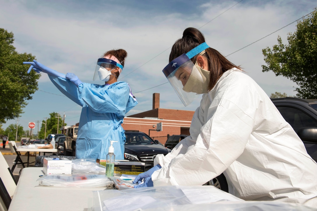 A worker puts on protective gear while another works at a table.