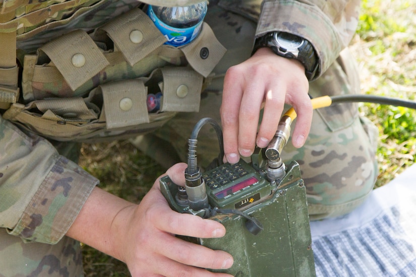 Two hands hold a military radio.