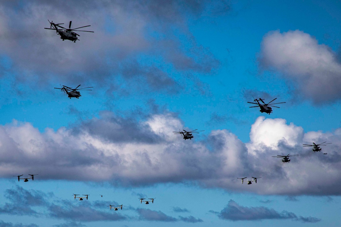 A group of Marine Corps aircraft fly through a cloudy sky.