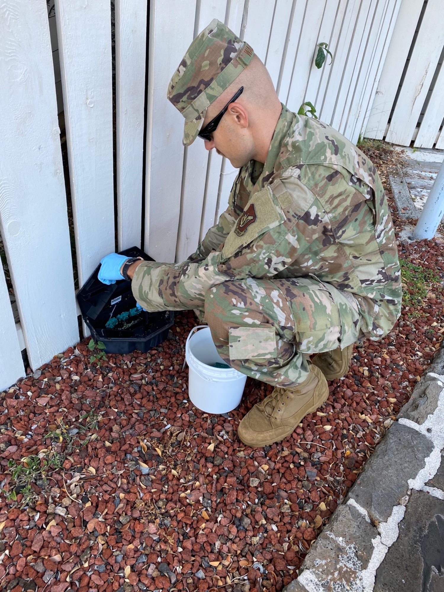 Senior Airman David Walker, 647th Civil Engineer Squadron pest management journeyman, refills the rodent bait stations around a building on Joint Base Pearl Harbor-Hickam, Hawaii, May 19, 2020. The bait attracts rodents to ensure the team can catch the pests before they enter JBPHH buildings. (Courtesy photo)