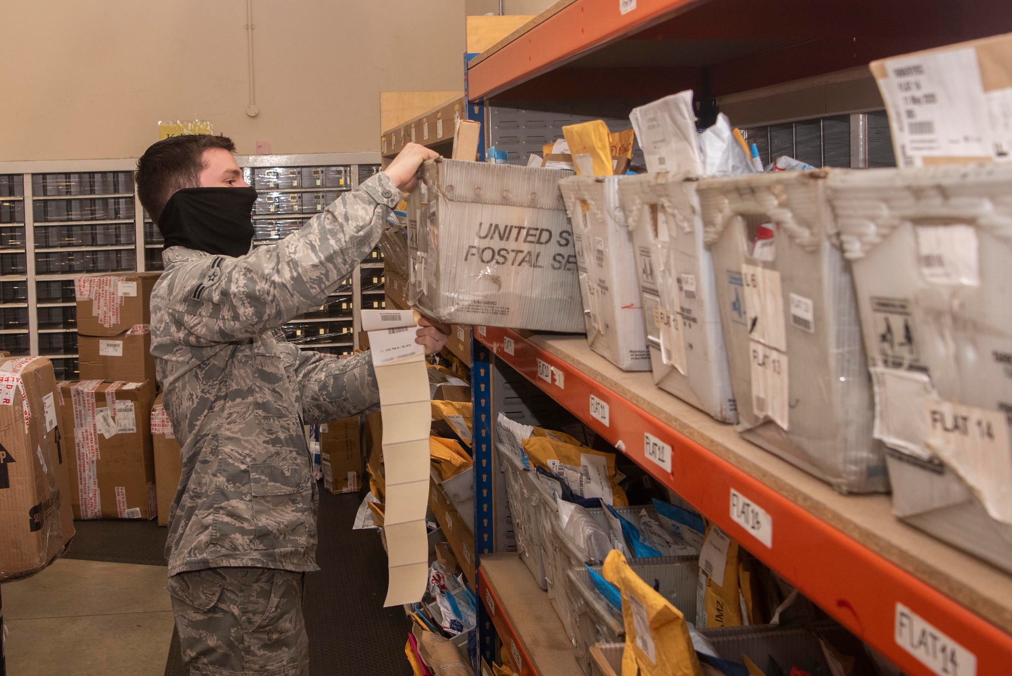 Airman 1st Class Austin Wells, 100th Force Support Squadron military postal clerk, shelves a basket of mail inside the post office at RAF Mildenhall, England, May 19, 2020. The post office has extended holding times for packages due to COVID-19. (U.S. Air Force photo by Airman 1st Class Joseph Barron) (Portions of this photo have been blurred for privacy purposes)