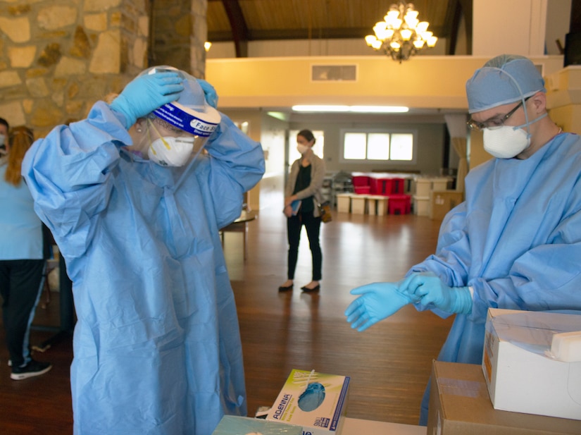 Spc Dominique Dalessio (left) and Sgt. Shane Brandes (right) adjust their face shields and personal protective equipment while preparing for the mission to administer COVID-19 tests at the Lancashire Hall Nursing and Rehab Center in Lancaster, Pa., on May 19, 2020.