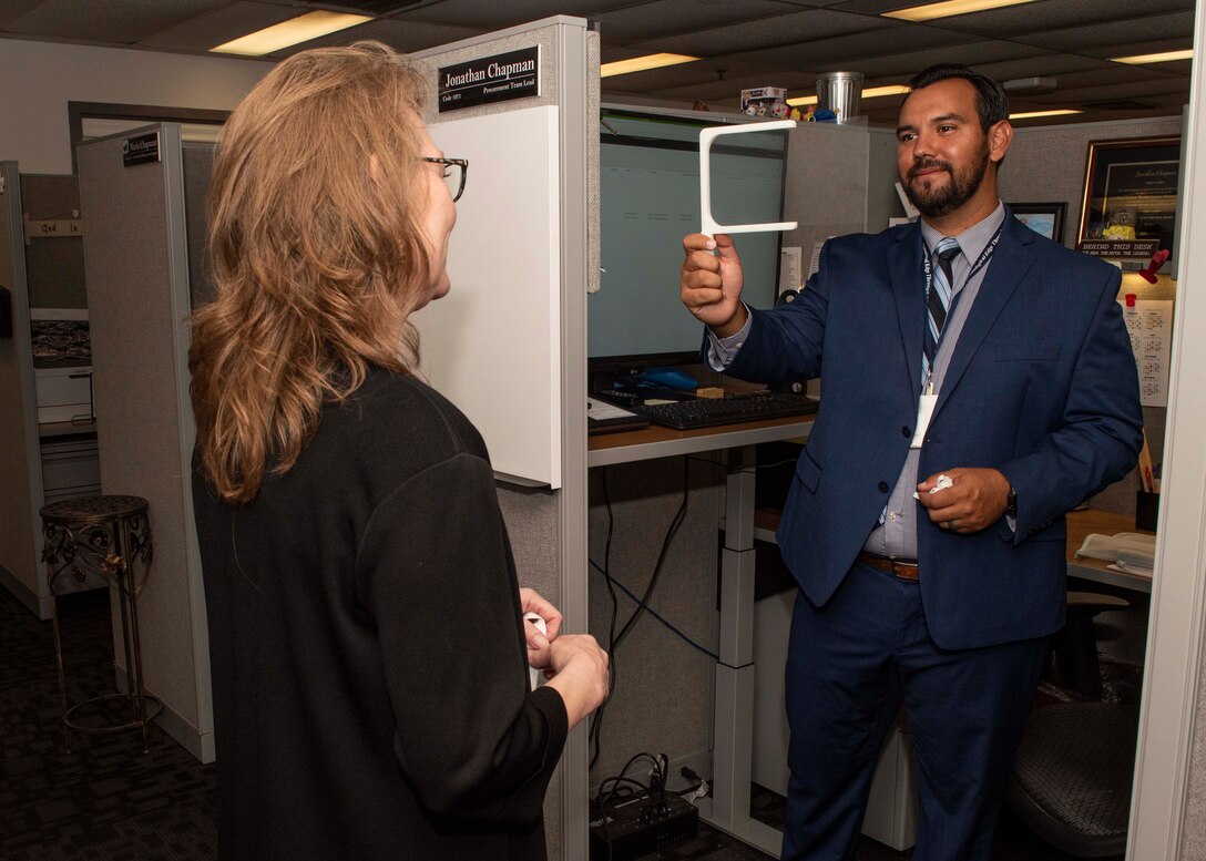 Jonathan Chapman, NSWC PCD procurement lead, speaks with Deanna Pedersen, NSWC PCD procurement branch head, using the lip reading kit he designed.  Chapman designed the kit for use by hearing impaired team members at the command.