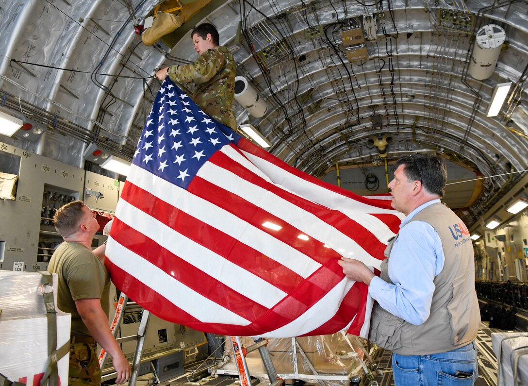 Brock Bierman, U.S. Agency for International Development assistant administrator, and U.S. Air Force Airmen hang an American flag above USAID ventilators to be delivered to Moscow, Russia, on a U.S. Air Force C-17 Globemaster III assigned to Joint Base Charleston, South Carolina, at Dover Air Force Base, Delaware, May 19, 2020. The COVID-19 outbreak is worsening in Russia, which has the second-highest number of cases in the world and the highest number of cases in Europe. The U.S. Government is responding with a donation of ventilators for the Russian people.. (U.S. Air Force photo by Senior Airman Christopher Quail)