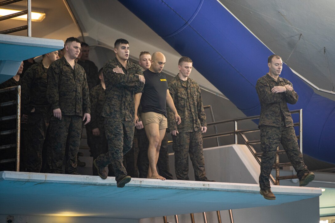 Marines and Sailors with Special Purpose Marine Air-Ground Task Force - Southern Command jump off a tower into a training pool during the basic swim qualification course at Marine Corps Base Camp Lejeune, North Carolina, March 11, 2020. The basic swim qualification course requires Marines to shed personal protective gear underwater, swim and float in full utilities for 4 minutes, jump from a tower, and swim 25 meters with their pack. Marines and Sailors with SPMAGTF-SC are conducting a variety of pre-deployment training events and qualifications prior to deploying in order to enhance crisis response readiness in and around Central America, South America and the Caribbean. These events are held at Camp Lejeune and will assist the Marines and Sailors with providing security cooperation training and engineering projects alongside partner nation military forces in the Latin American and Caribbean region, as well as remaining ready to respond to crises in the event of an emergency within the region. (U.S. Marine Corps photo by Sgt. Andy O. Martinez)