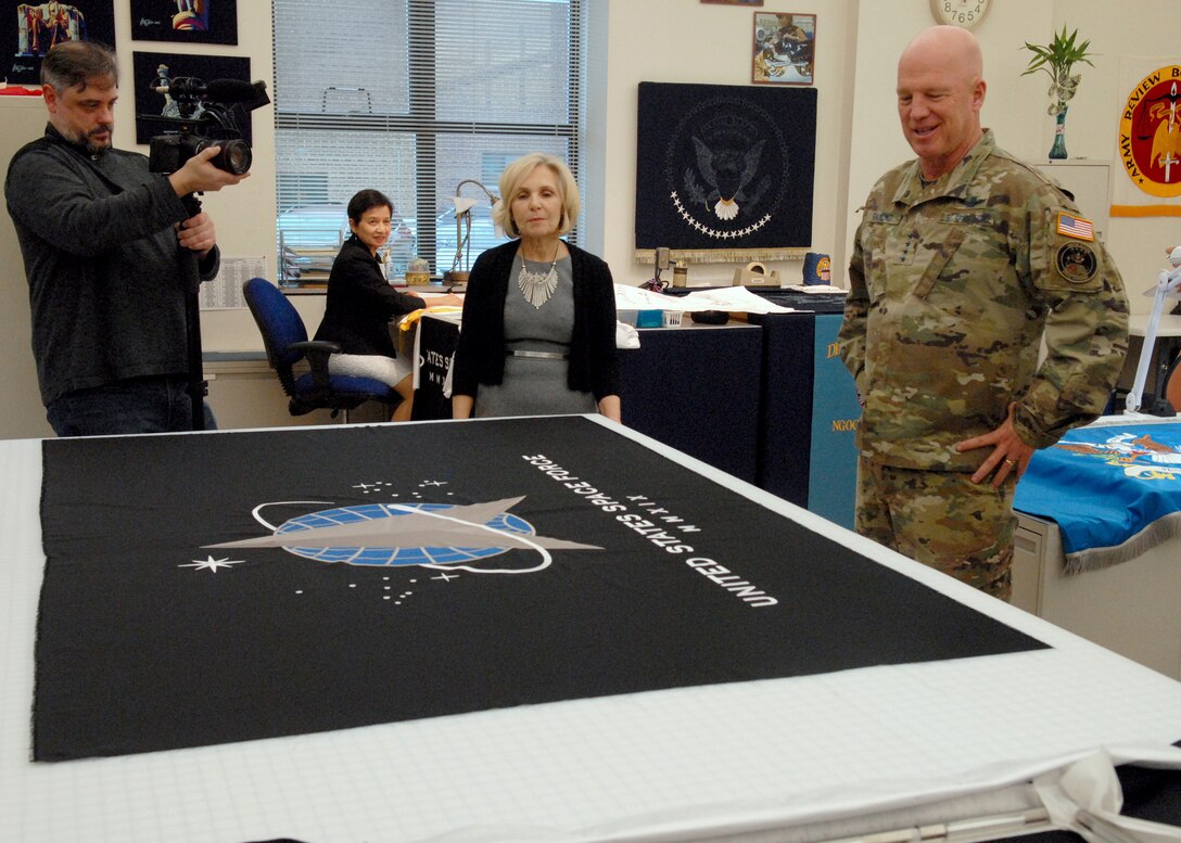 Flag room Supervisor Linda Farrell explains an embroidered flag of the Space Force flag to U.S. Space Force Commander Gen. John W. “Jay” Raymond