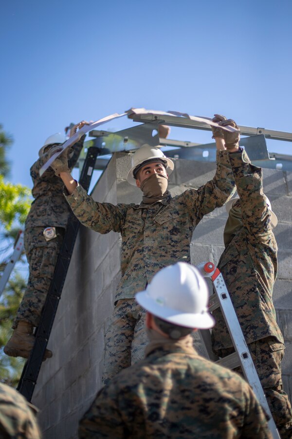 Lance Cpl. Ian Garcia, a combat engineer with Special Purpose Marine Air-Ground Task Force - Southern Command, holds a roof panel overhead while fellow engineers get into place during a general exercise at Marine Corps Base Camp Lejeune, North Carolina, April 17, 2020.The GENEX includes training events such as engineering projects and evacuation control center training scenarios that will help build the SPMAGTF-SC for their final certification exercise. These training events also provide the Marines and Sailors with real-world scenarios to prepare them for their deployment to assist partner nation militaries in Latin America and the Caribbean. Garcia is a native of Wilsonville, Oregon. (U.S. Marine Corps photo by Cpl. Benjamin D. Larsen)