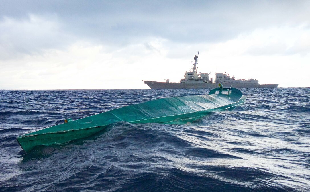 A Coast Guard boarding team in a boat approach a low profile semi-submersible.