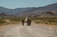 Airmen from the 99th Contracting Squadron dress in their OCPs march down a dirt path in the summer Nevada sun with mountains in the background.