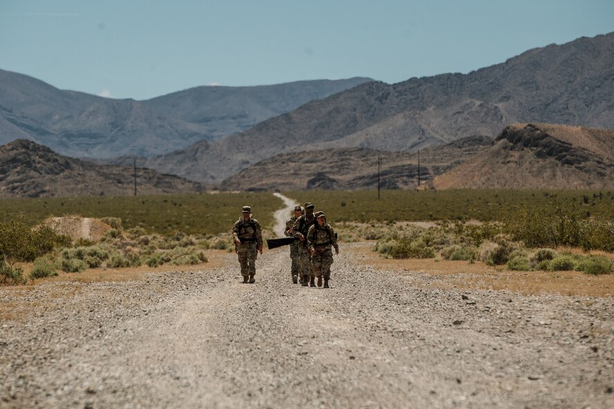 Airmen from the 99th Contracting Squadron dress in their OCPs march down a dirt path in the summer Nevada sun with mountains in the background.