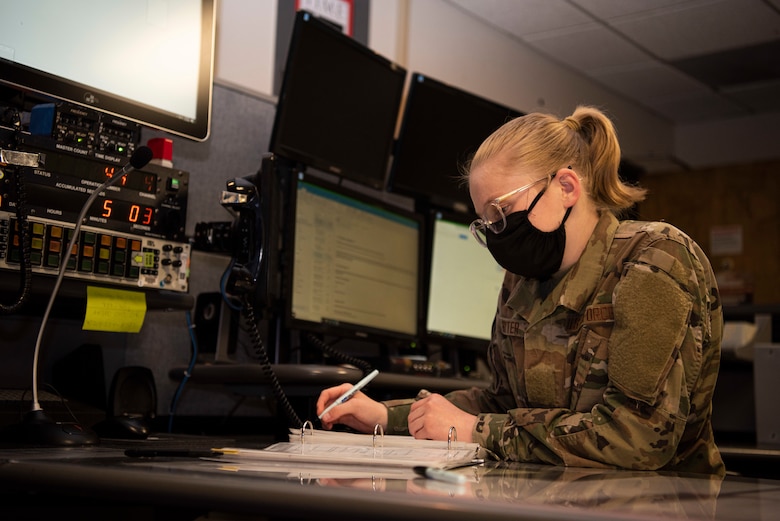 Airman Basic Julia Hitter, 30th Space Wing Command Post junior emergency actions controller, goes through a shift changeover checklist May 18, 2020, at Vandenberg Air Force Base, Calif. During the COVID-19 pandemic, the 30th SW Command Post has taken on the responsibility of creating daily situation reports for the U.S. Air Force and Space Force that detail the status of Vandenberg AFB and the response the base is taking towards COVID-19, on top of their every-day workload. (U.S. Air Force photo by Senior Airman Hanah Abercrombie)