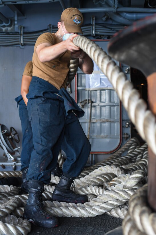 Two sailors handle rope aboard a naval vessel.