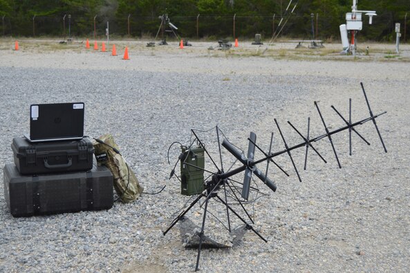 A laptop, tactical radio, satellite antenna and carrying cases sitting outside.