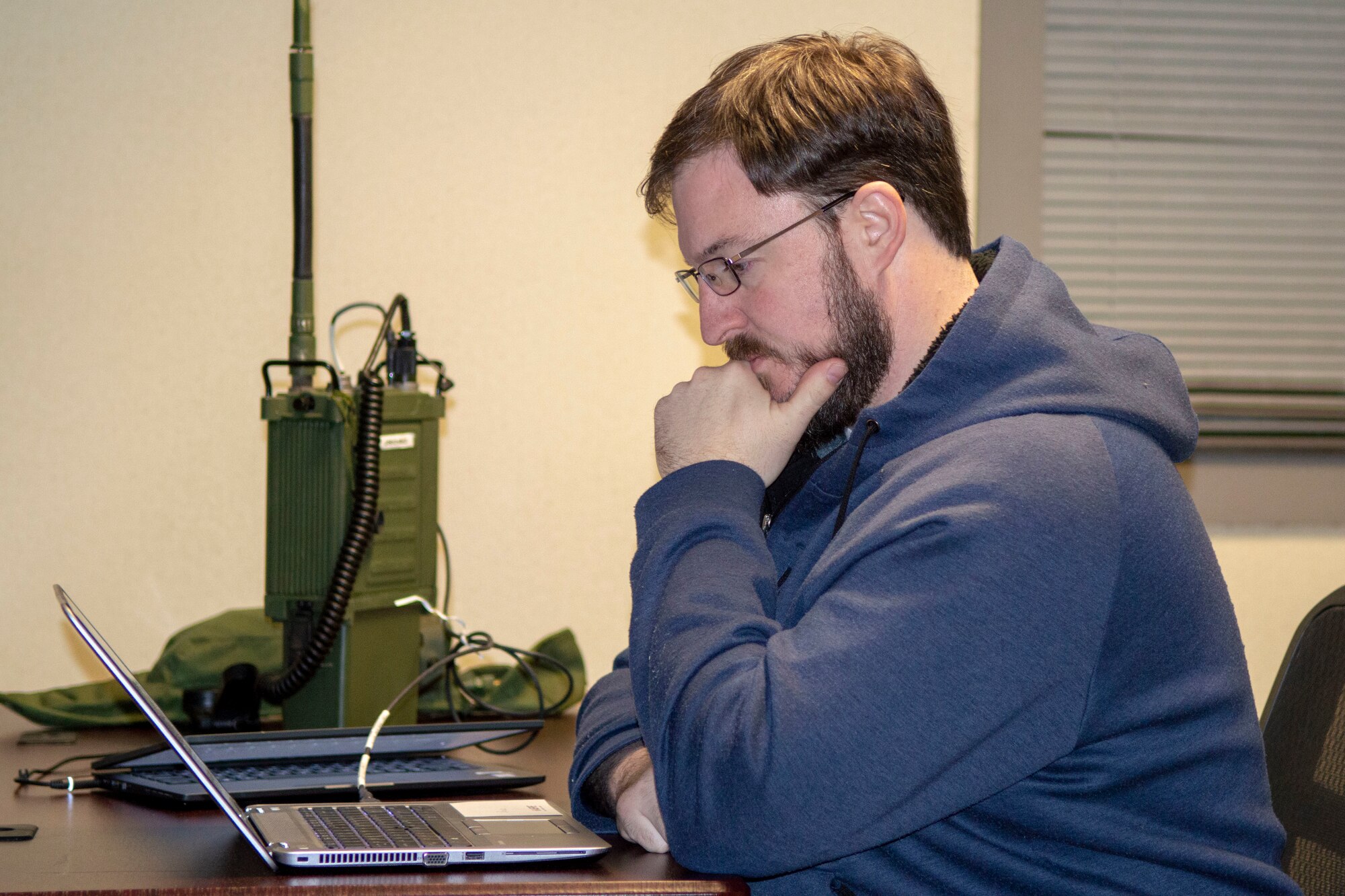 Man sitting in front of laptop with tactical radio on table.