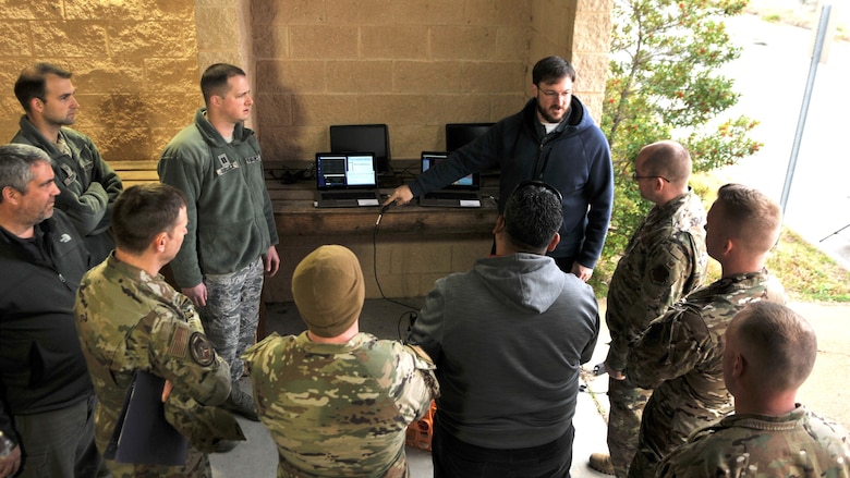 Airmen standing in front of laptops outside.