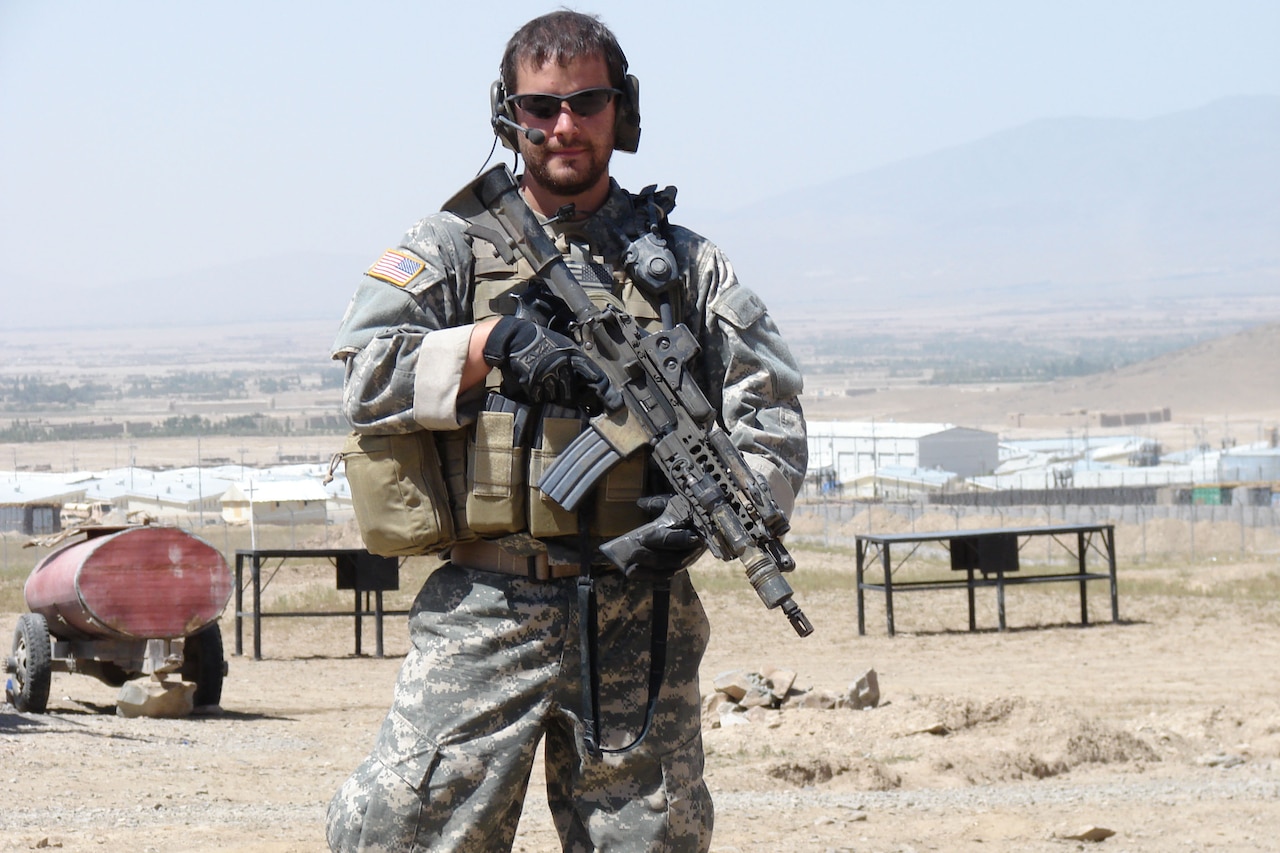 A soldier poses with his weapon in a desert town.