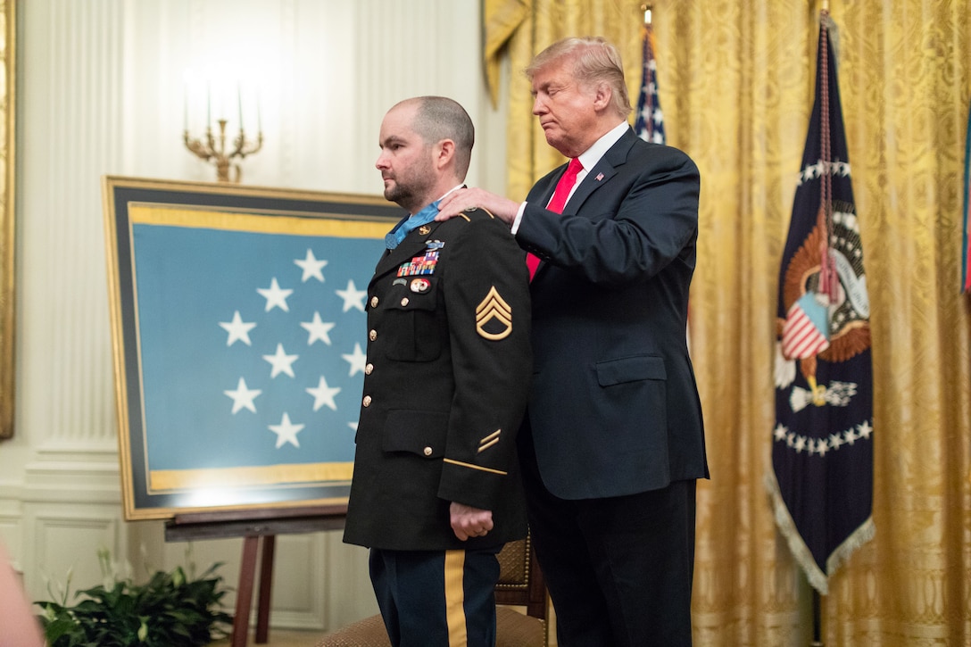 A man places a medal around a uniformed man’s neck.