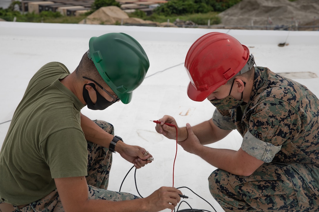 Two Marines wearing hardhats examine a wire.