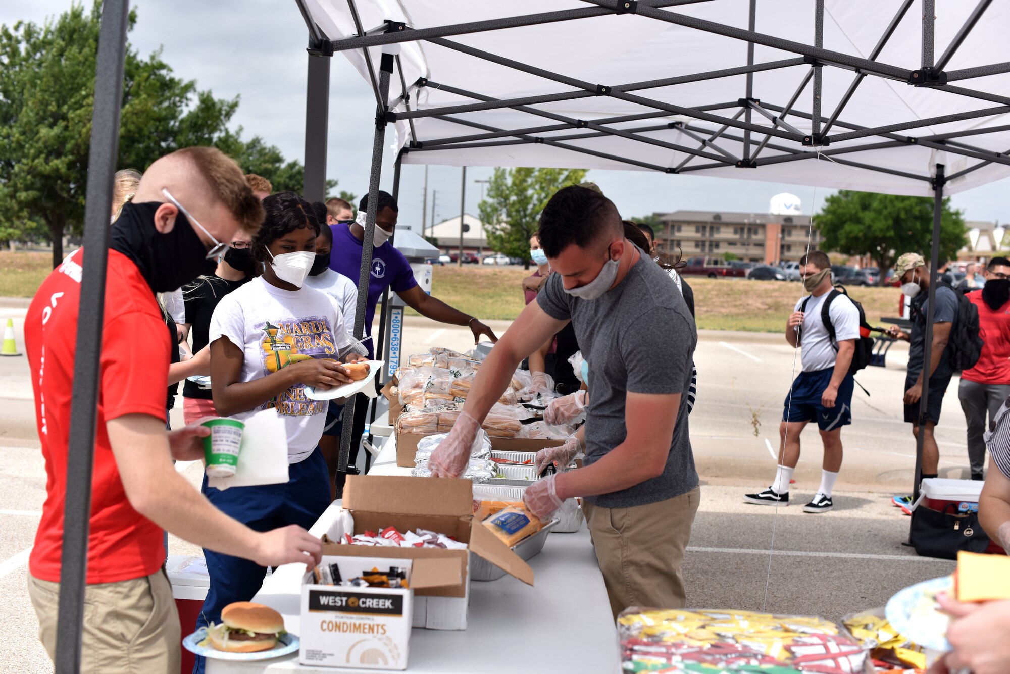 Goodfellow students go down the serving line receiving their hotdogs and hamburgers during the Memorial Day BBQ at the Crossroads on Goodfellow Air Force Base, Texas, May 23, 2020. While observing guidelines from the Centers for Disease Control and Prevention students spent time outside talking with chapel personnel and first sergeant members. (U.S. Air Force photo by Senior Airman Seraiah Wolf)