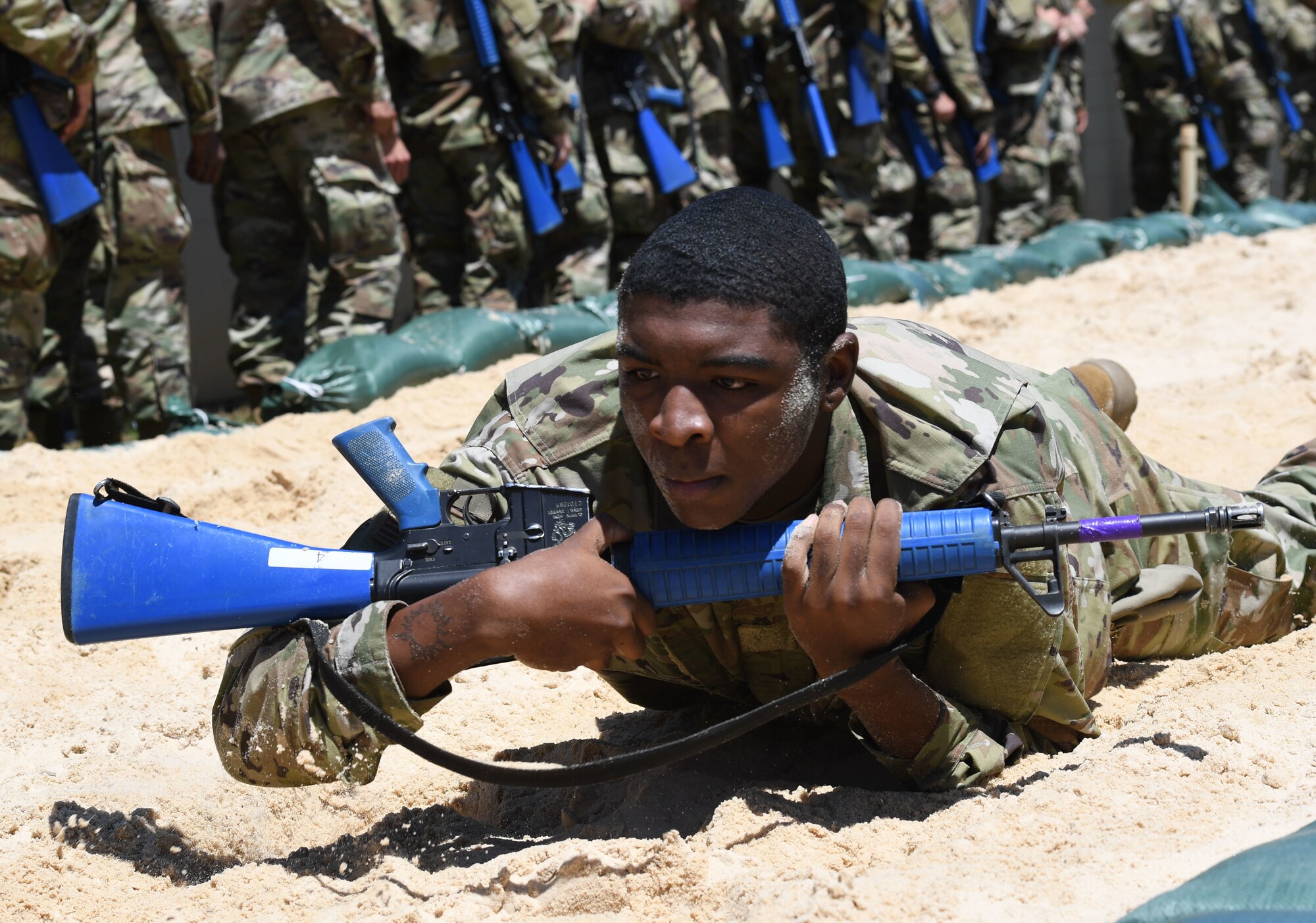 Airmen crawls in sand with rifle