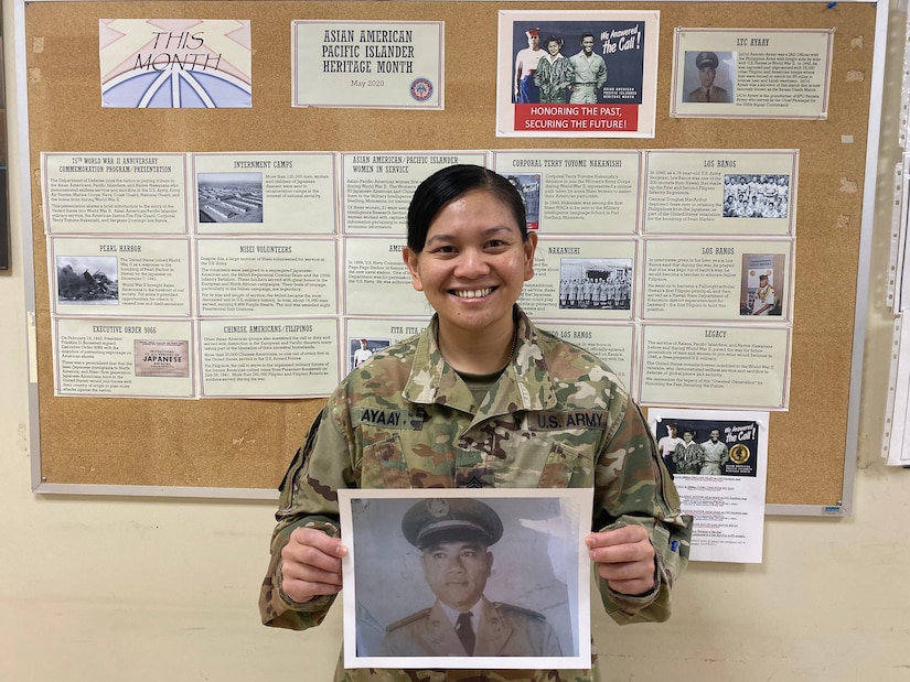 Sergeant First Class Pamela Ayaay holds a photo of her late grandfather, Lieutenant Colonel (RET) Antonio Ayaay, in front of the 160th Signal Brigade Equal Opportunity Board for Asian Pacific Islander Heritage Month.