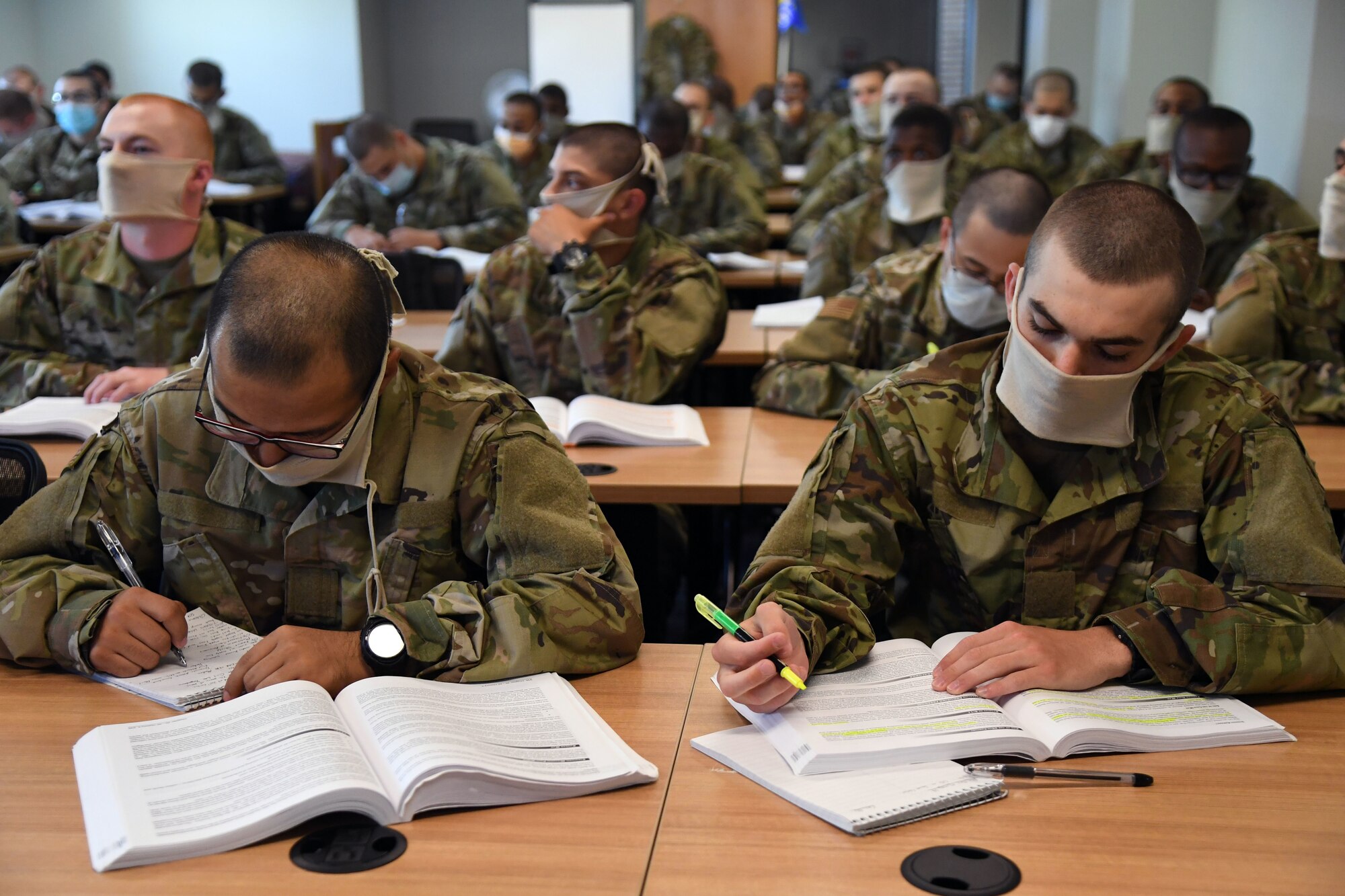 Airmen wearing masks sit in class