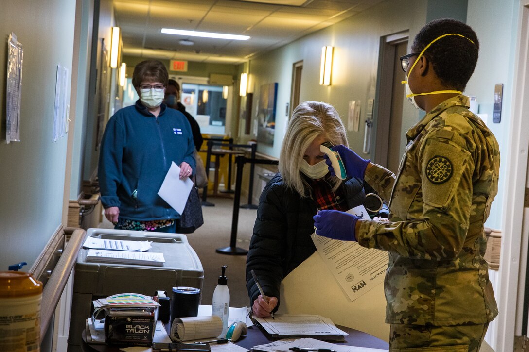 A guardsman takes a health care worker’s temperature.