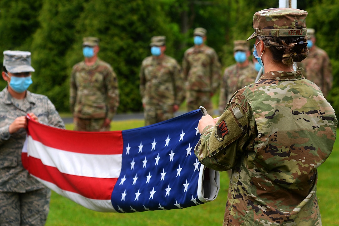 Airmen in masks fold a flag at a retreat ceremony.