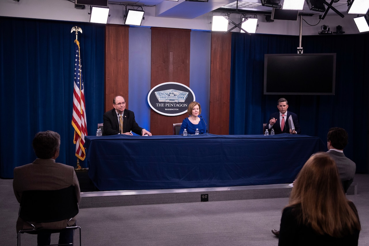 Three civilians speak at a table.