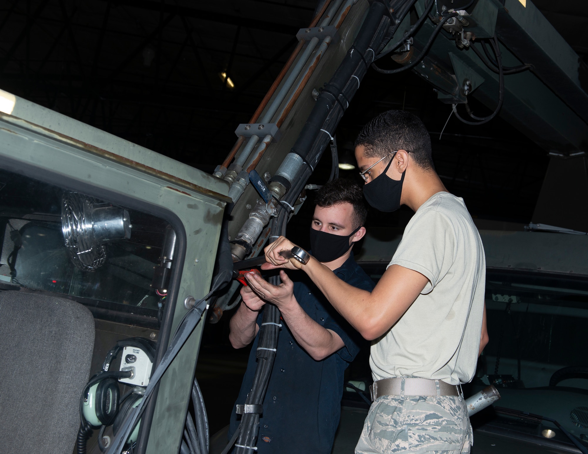Two Airmen working on fly-cab of a deicer, turning wrenches