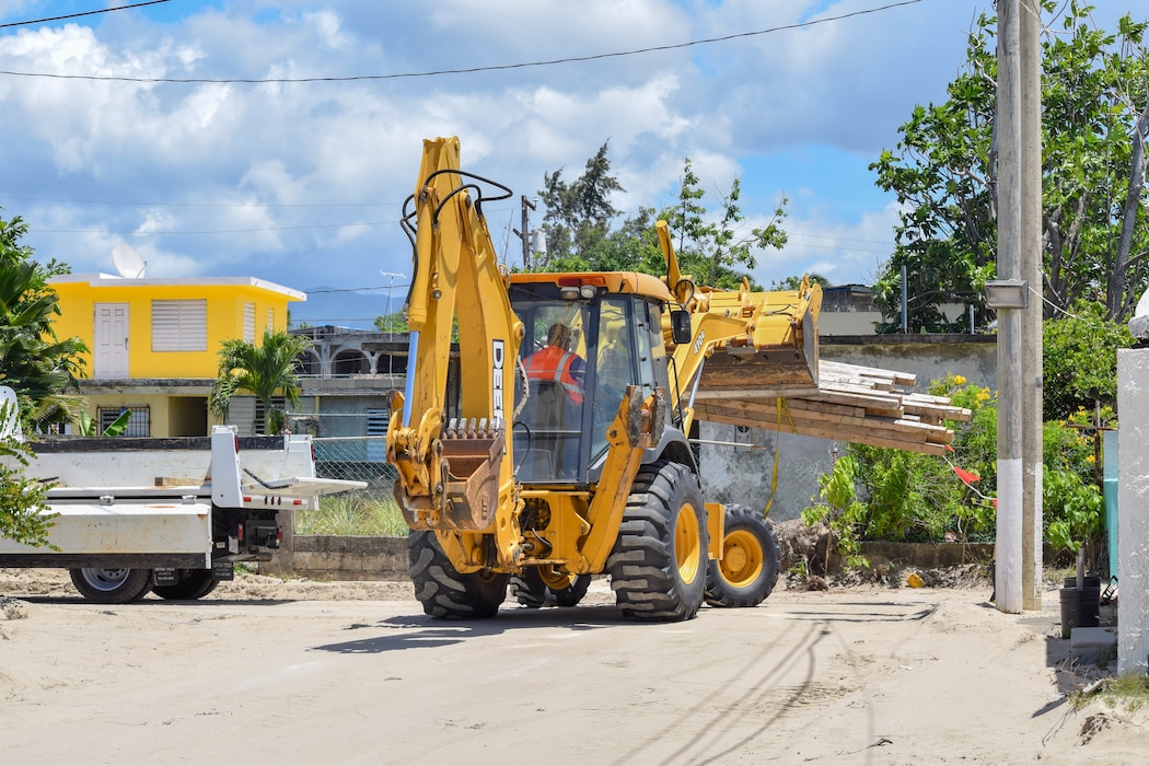 Yellow backhoe loader transporting logs