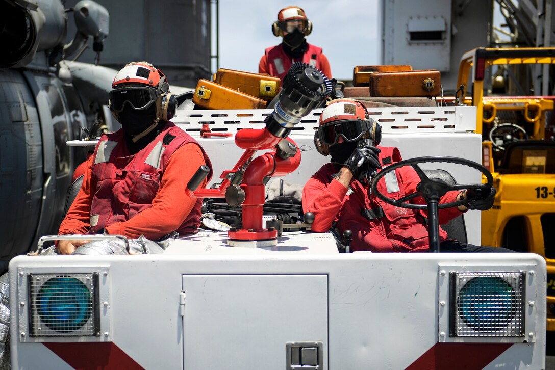 Three service members wear face masks, goggles and helmets as they watch flight operations on the deck of the USS Theodore Roosevelt.