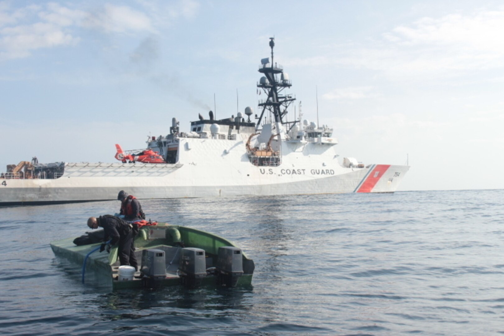 A low-profile go-fast vessel is shown next to the Coast Guard Cutter James.