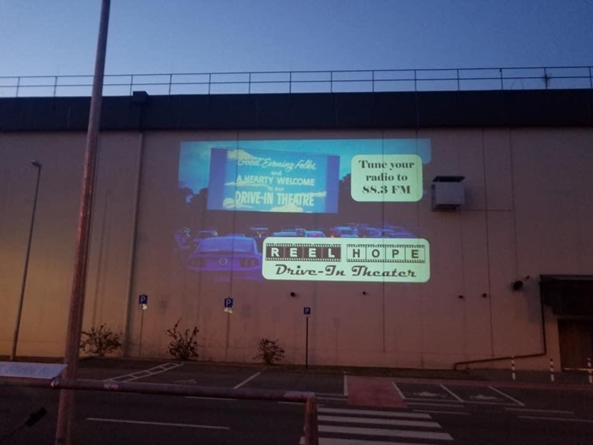 A projector displays radio directions to the crowd attending the ‘Reel Hope Drive-in’ theater Apr. 25 at Ramstein Air Base, Germany. Chaplain Portmann Werner, 693rd Intelligence, Surveillance, and Reconnaissance Group’s head chaplain, converted the outside of their group’s building and parking lot into the theater. (Courtesy Photo)