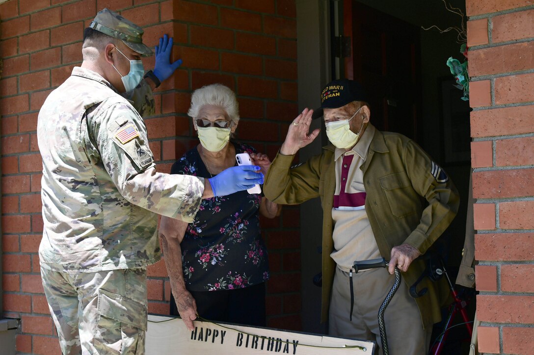 A solider holds a phone while showing a retired soldier his family.