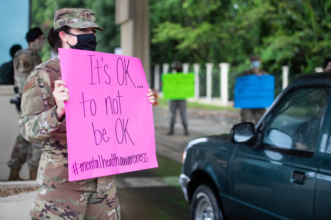 Airman holds up sign that says, it's OK, to not be OK, outside the Day Street gate.