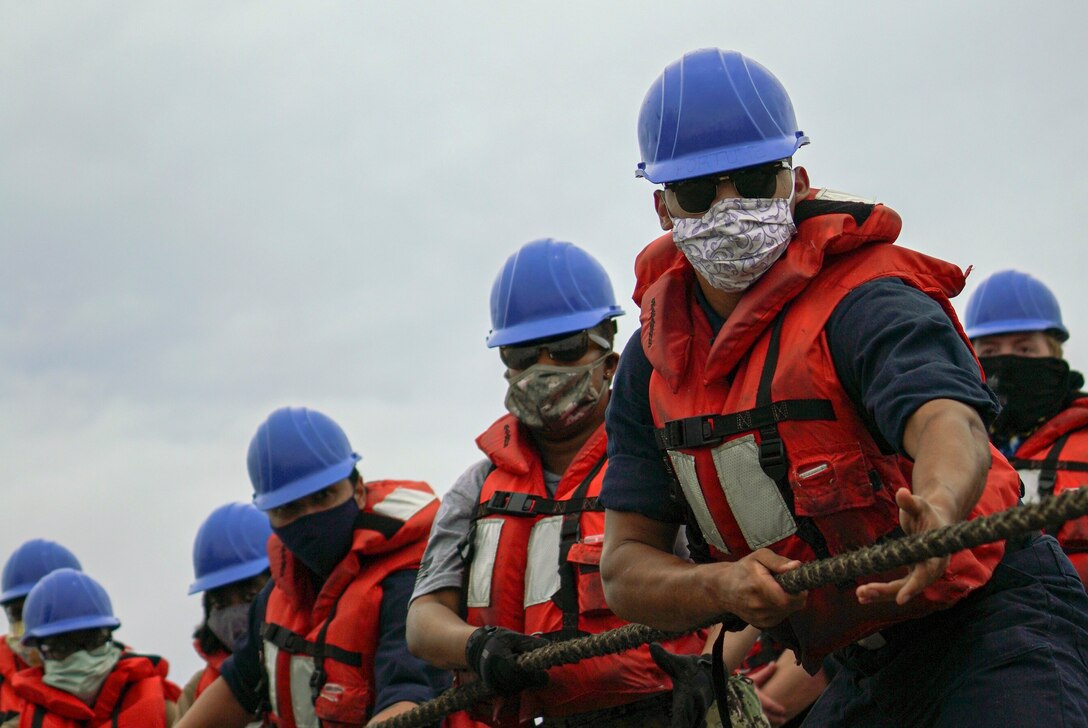 Sailors in protective gear pull a rope.